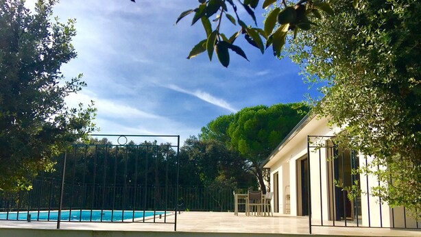 A pool area with a clear view of the sky and trees, a white building, and a metal gate. - PRETTY NEW AIR CONDITIONED VILLA WITH HEATED POOL IN THE CAMPAIGN OF UZES (UZES)