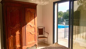 A room with a wooden wardrobe, a chair, a patterned rug, and a sliding glass door leading to an outdoor swimming pool. - PRETTY NEW AIR CONDITIONED VILLA WITH HEATED POOL IN THE CAMPAIGN OF UZES (UZES)