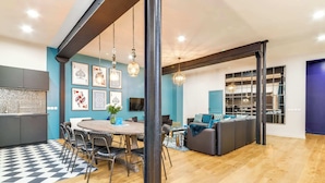 A modern kitchen with a black and white checkered floor, a dining area with a round table and chairs, and a living area with a sofa and a TV.