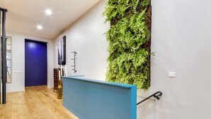 A modern hallway with a wooden floor, a blue reception desk, a wall-mounted green plant wall, and a door leading to another room.