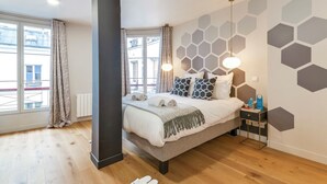 A modern bedroom with a bed, bedside tables, a large window, and a geometric wall design.