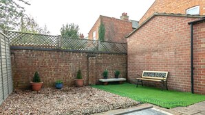 A backyard with a brick wall, a wooden bench, and potted plants. - Portobello House Newark (Newark)