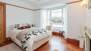 A bedroom with a large bed, a chair, a small table, and a window with curtains. - Portobello House Newark (Newark)