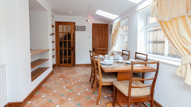 A dining area with a wooden table set for four, surrounded by chairs, a window with curtains, and a tiled floor. - Portobello House Newark (Newark)