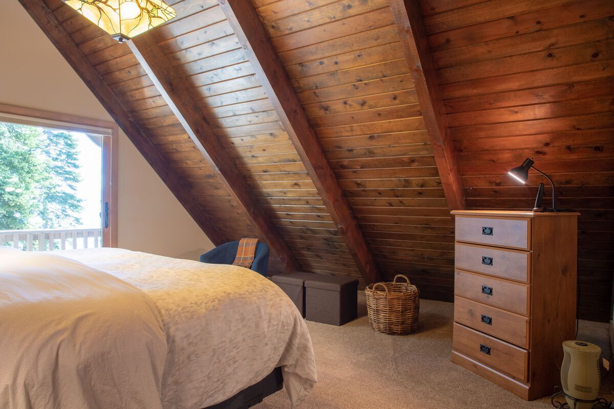 A bedroom with a sloped ceiling, a bed, a dresser, a lamp, and a basket.