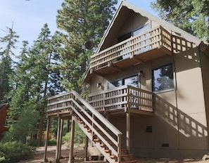 A two-story cabin with a wooden staircase and balcony, surrounded by trees. - Exquisite, fully remodeled lake view home! When only the best will do! (Carnelian Bay)