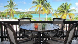 A round table with four chairs, two mugs with designs, and a view of the ocean with palm trees. - Your Perfect Beachfront Condo in Paradise - Sapphire Beach (Smith Bay)