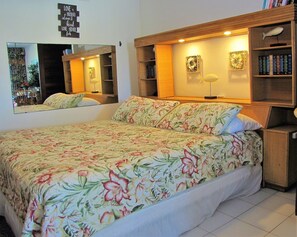 Un dormitorio con colcha estampada, un espejo grande, mesitas de noche con lámparas y una estantería.