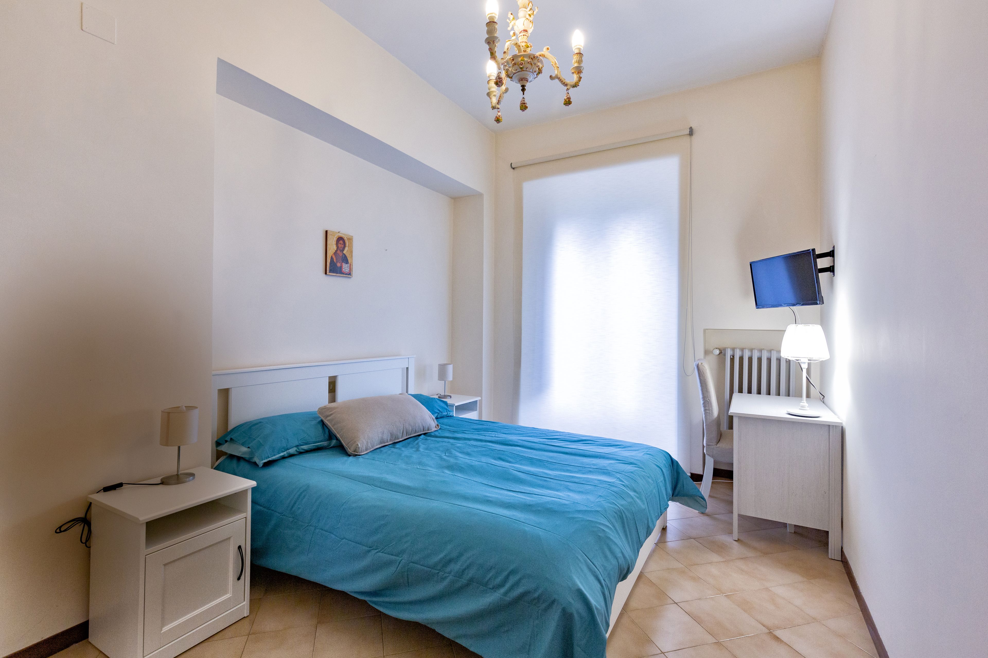 Un dormitorio con cama, mesita de noche, escritorio, silla y televisor.
