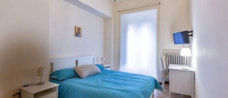 Un dormitorio con cama, mesita de noche, escritorio, silla y televisor.