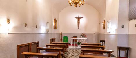 Interior de iglesia con bancos de madera, un crucifijo, una araña y suelo a cuadros.