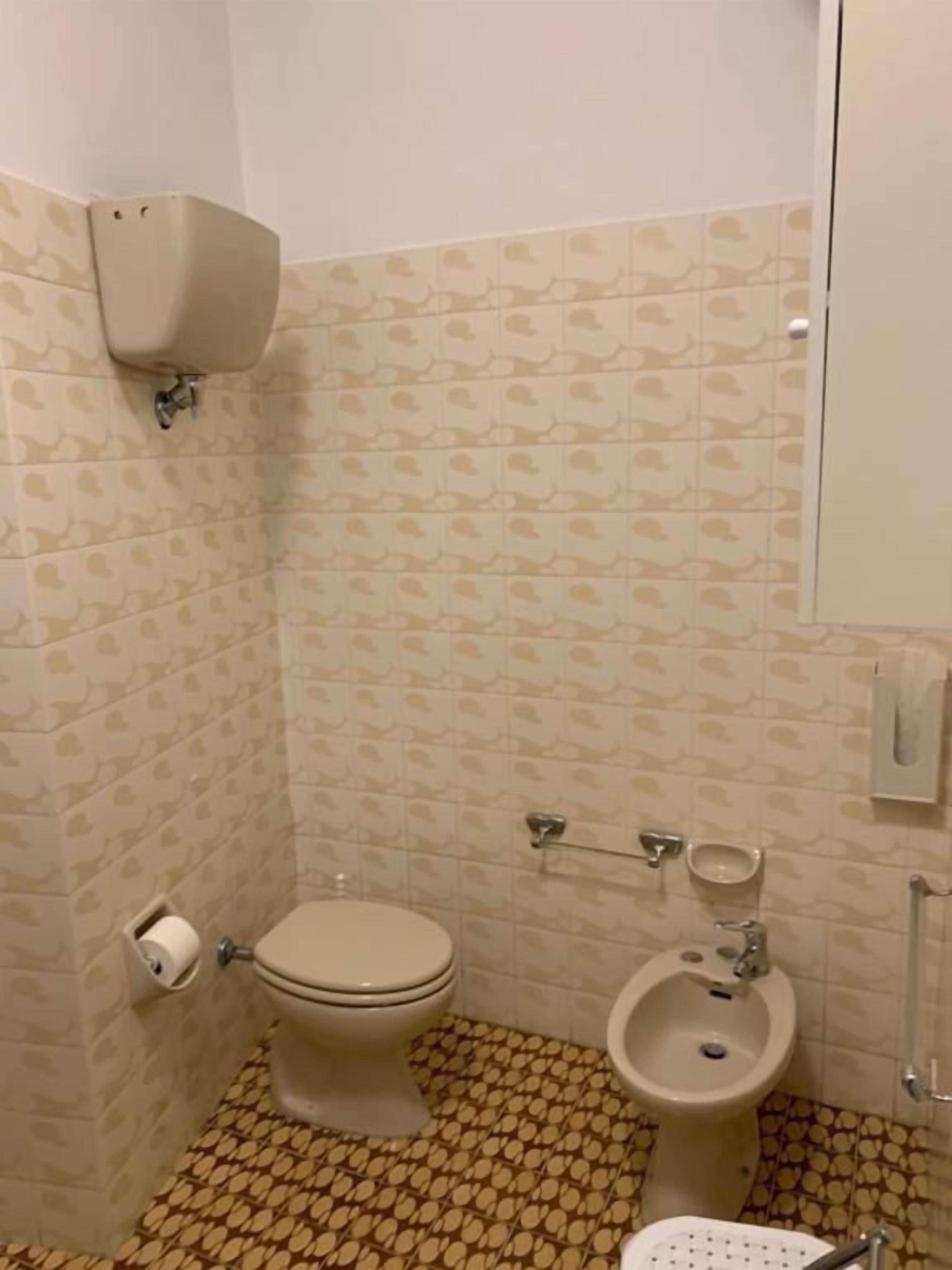 A small bathroom with a toilet, bidet, and a toilet paper holder.