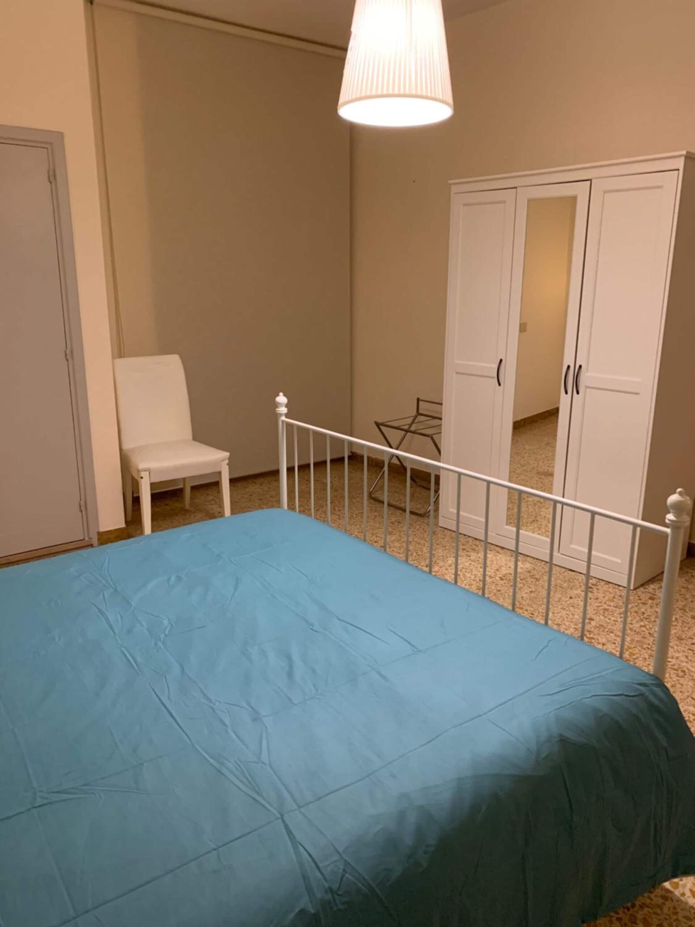 A bedroom with a bed, a chair, a wardrobe, and a hanging light fixture.