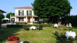 A two-story building with a balcony, outdoor seating, and a garden area with tables and chairs. - Villa Le Rose (Cavour)