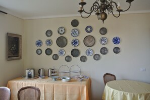 A dining area with a table set for two, a chandelier, and a wall decorated with various plates. - Villa Le Rose (Cavour)