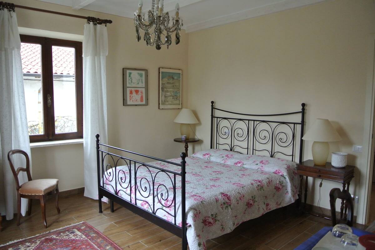 Un dormitorio con cama, una silla, una araña y dos lámparas de pared.