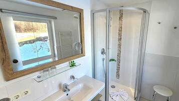 A bathroom with a glass-enclosed shower, a large mirror, and a white sink with a glass shelf.