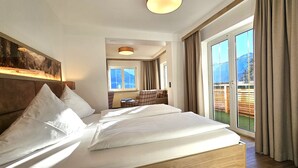 A hotel room with a large bed, a view of the outdoors, and a dining area. - Naturhotel Waldesruhe (Oberstdorf)