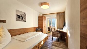 Un dormitorio con cama de madera, cabecera, mesita de noche, una silla, un escritorio, ventana con cortinas e imagen colgada en la pared.