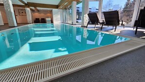 An indoor swimming pool with clear water, wooden beams, and lounge chairs. - Naturhotel Waldesruhe (Oberstdorf)