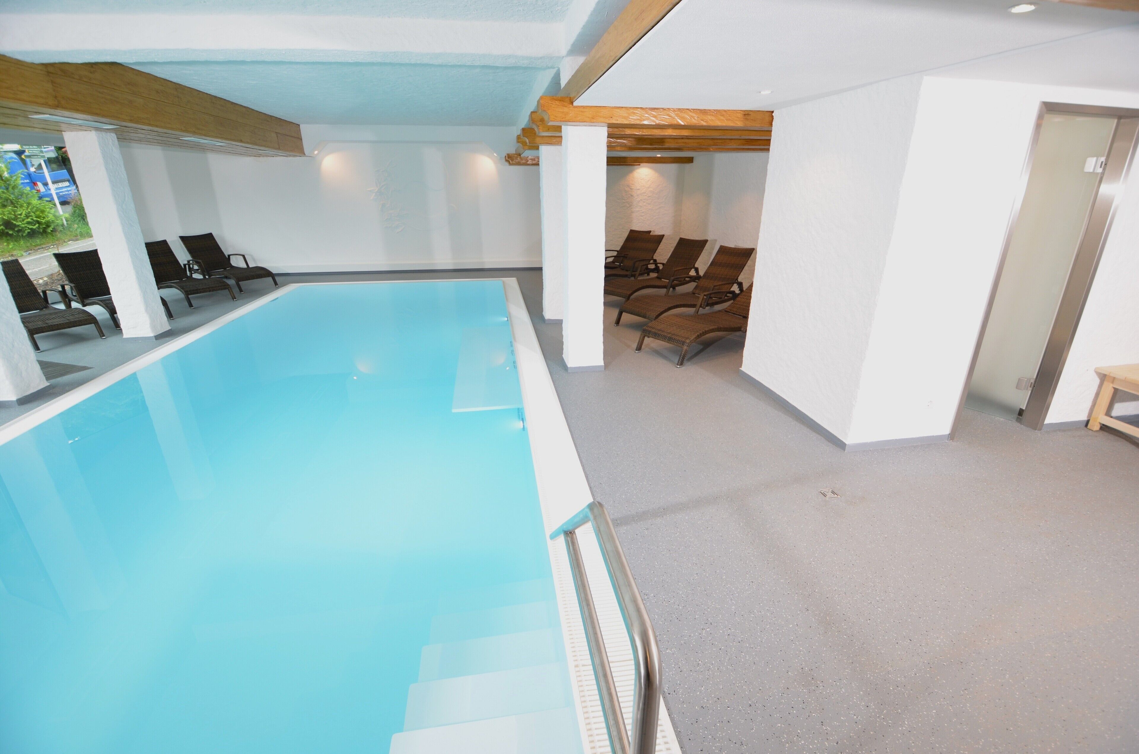 Una piscina interior con sillones de descanso y techo de estructura de madera.