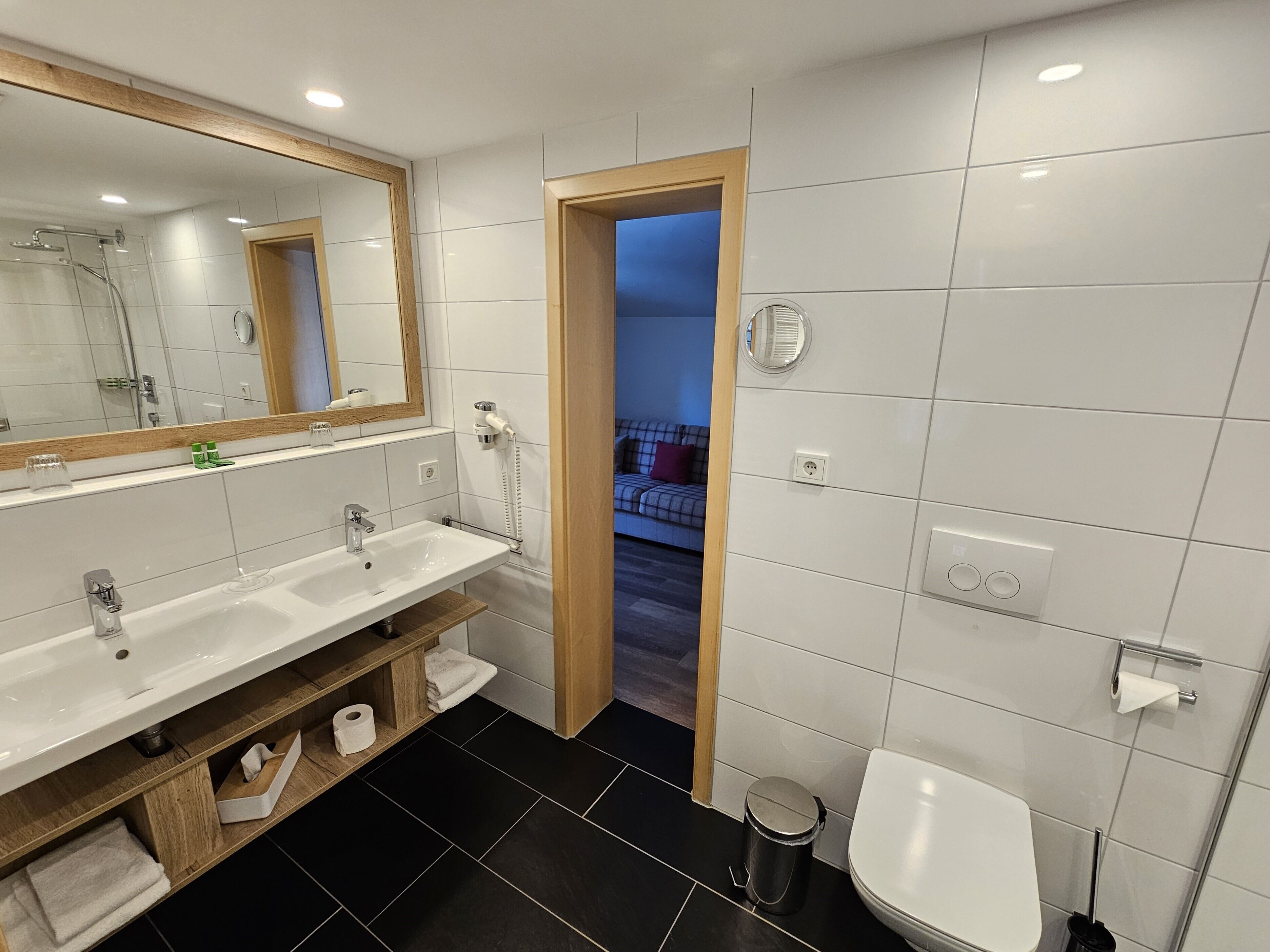 A modern bathroom with a double sink, a toilet, and a shower area.