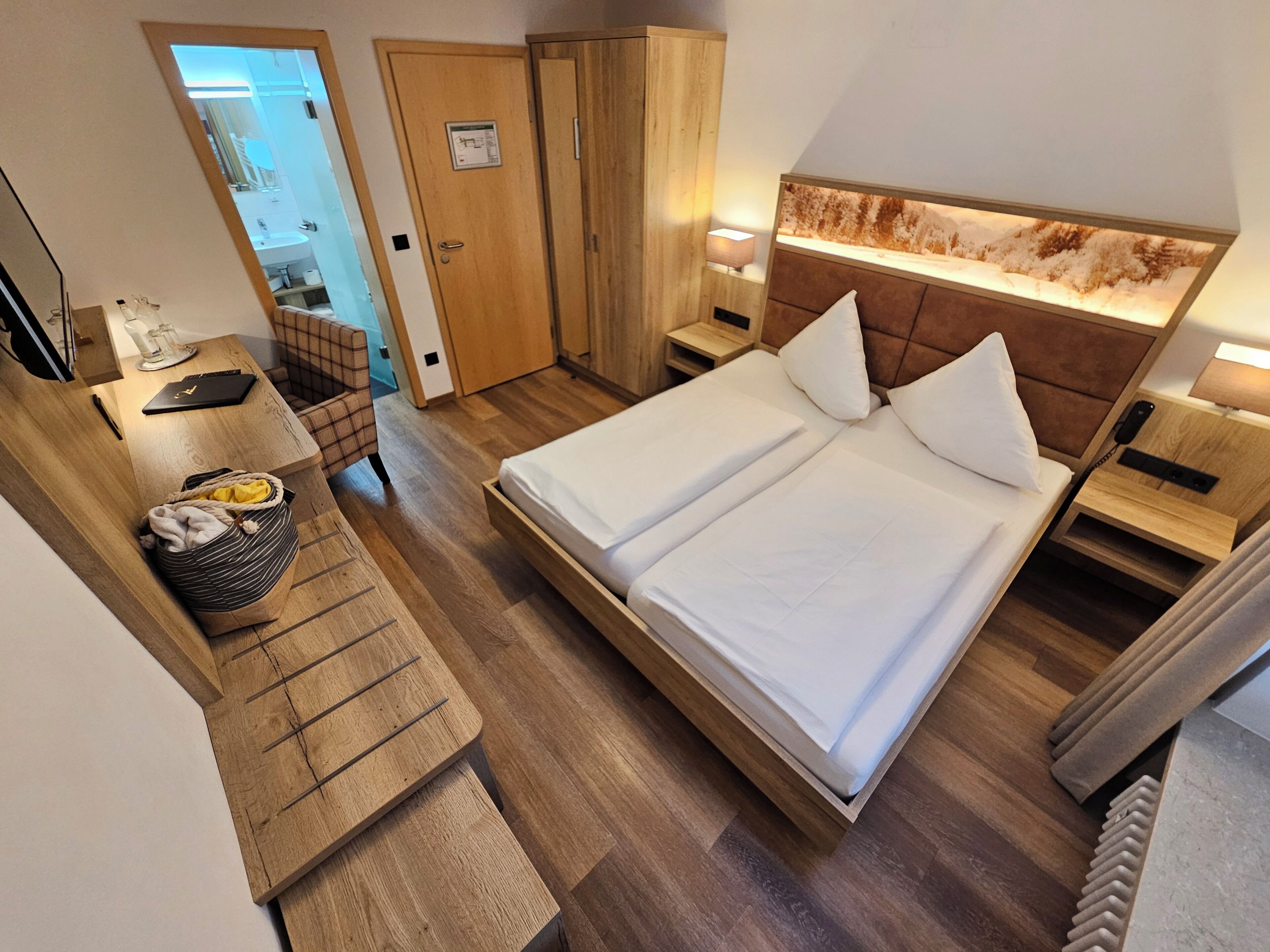 A hotel room with a bed, bedside tables, a desk, a chair, and a wardrobe.
