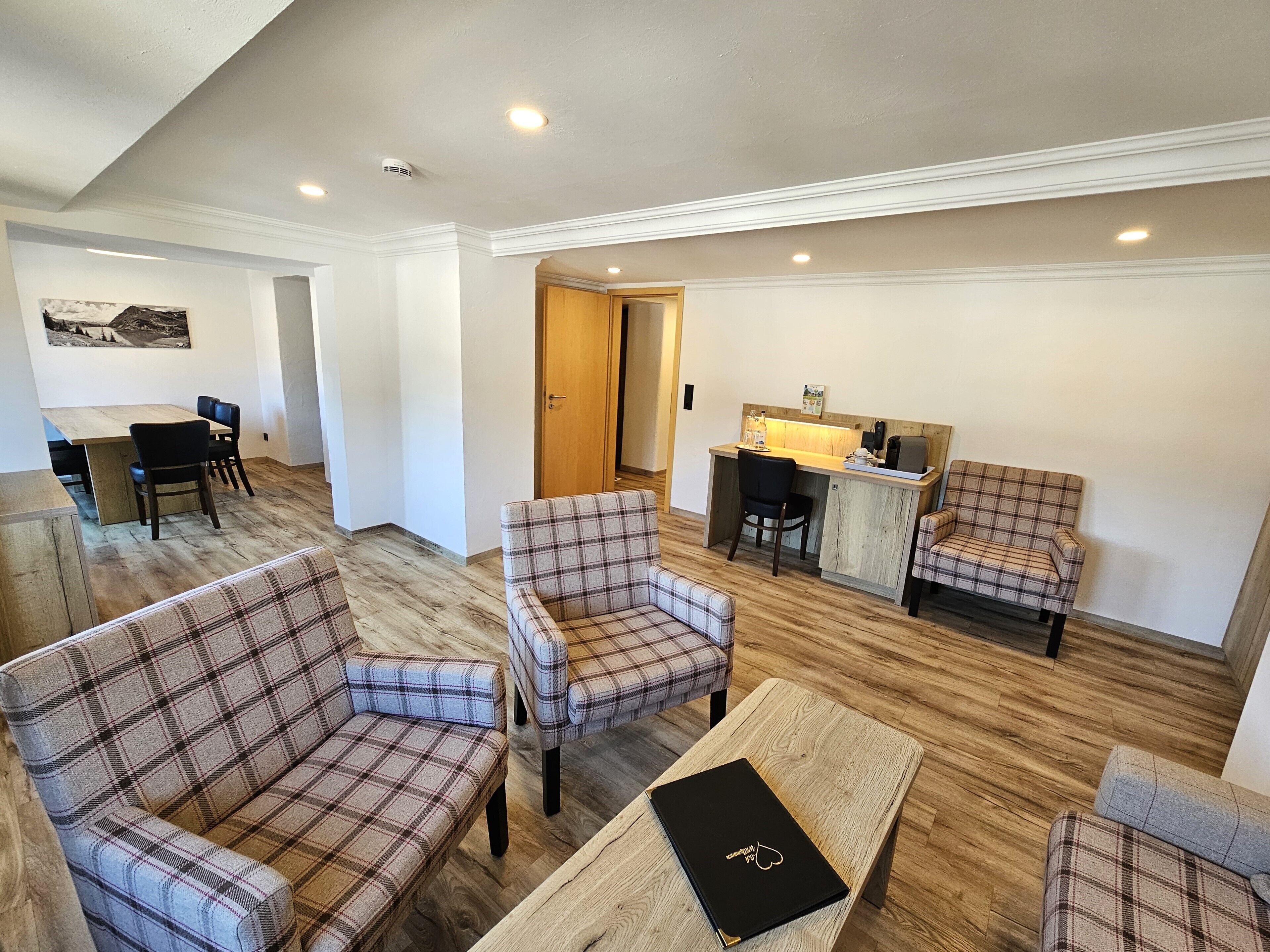 Uma sala de estar ampla, com sofás xadrez, uma mesa de centro de madeira e uma área de jantar com mesa e cadeiras.