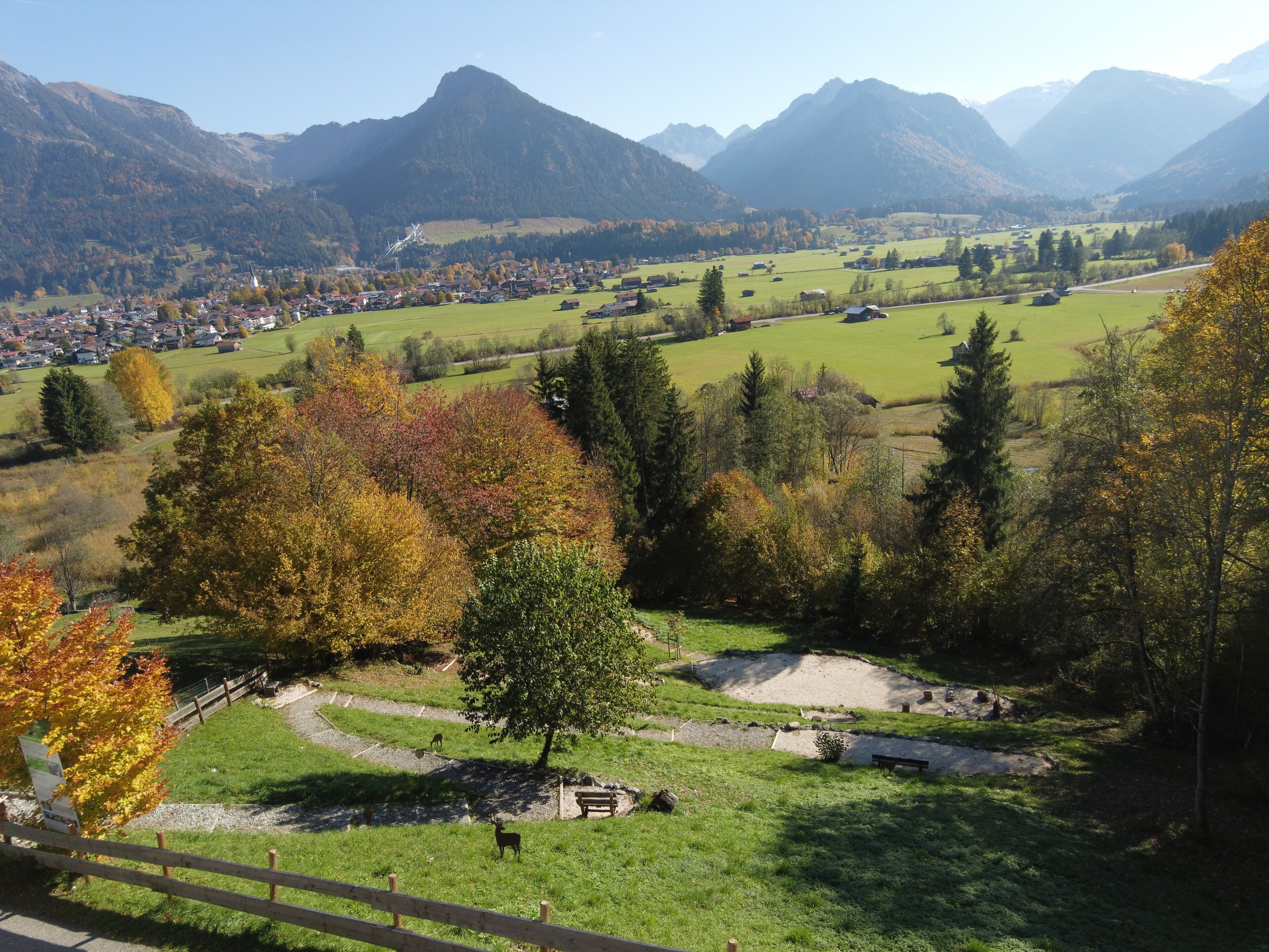 A scenic view of a mountainous area with a village, green fields, and autumn trees.