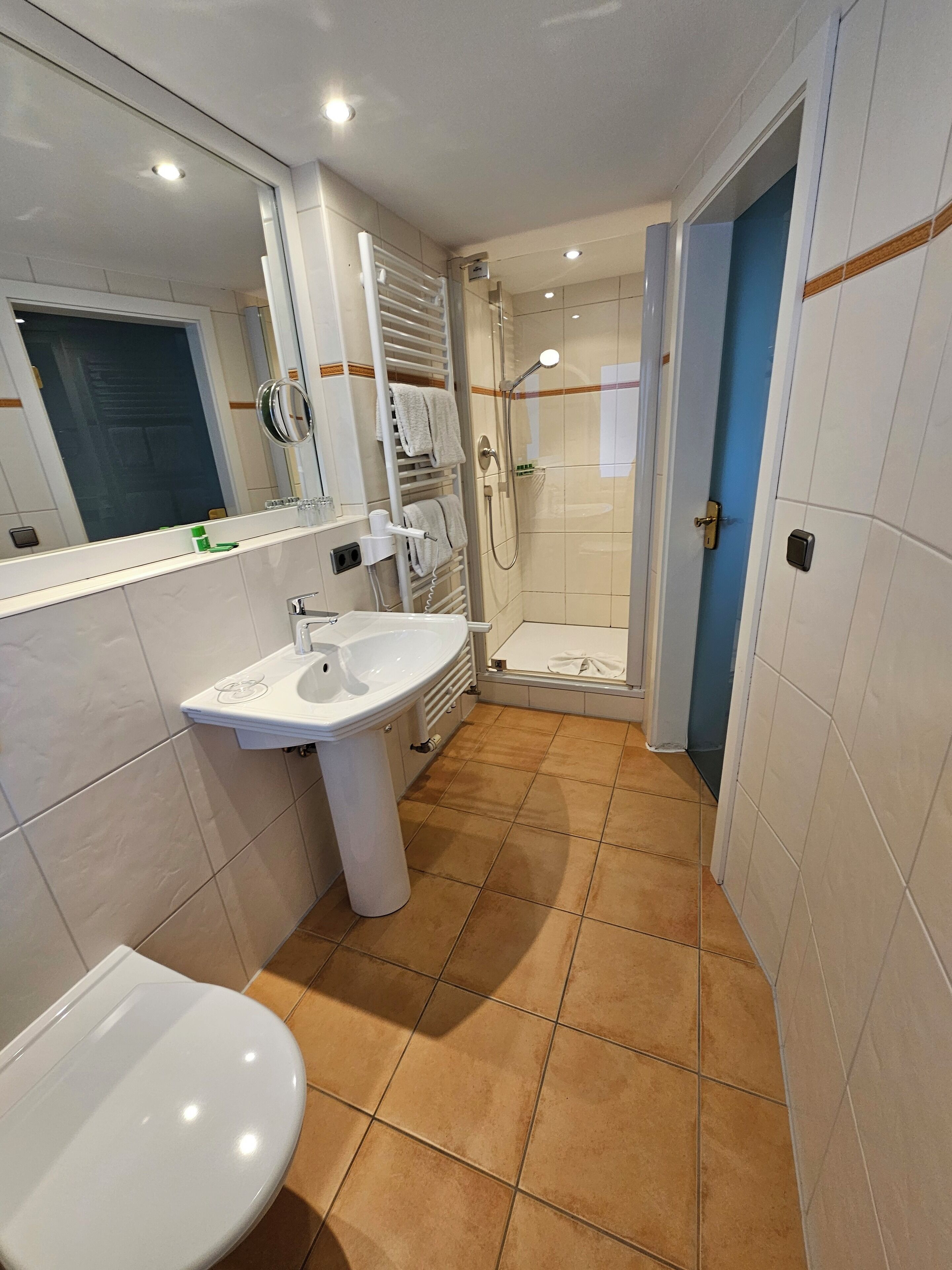 Un baño con lavabo, espejo, toallero, ducha e inodoro.