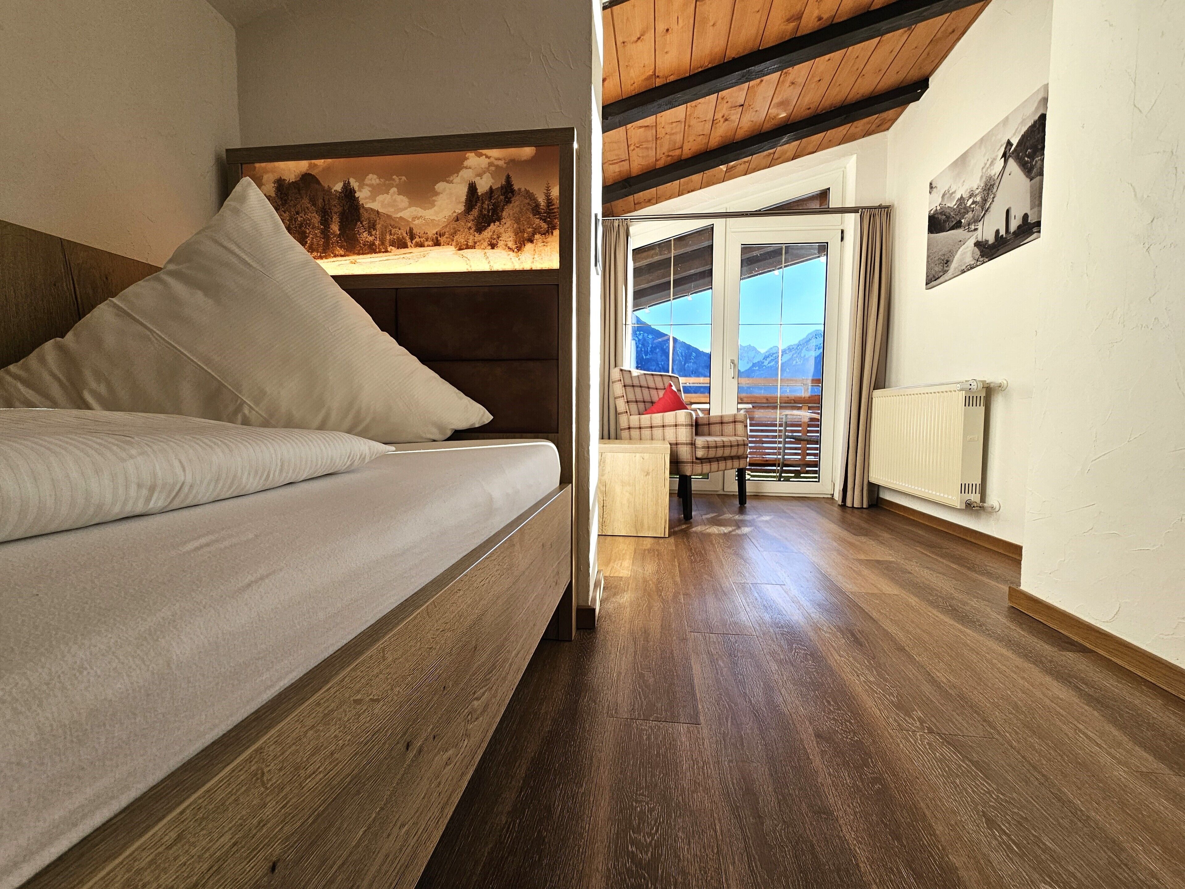 A room with a bed, a wooden ceiling, a view of mountains through a glass door, and a radiator on the wall.