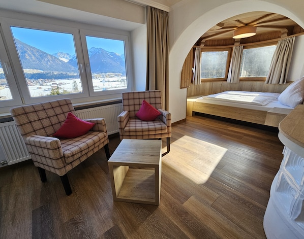 Una habitación acogedora con una cama, dos sillones a cuadros, una mesita y amplios ventanales con vistas a la montaña.