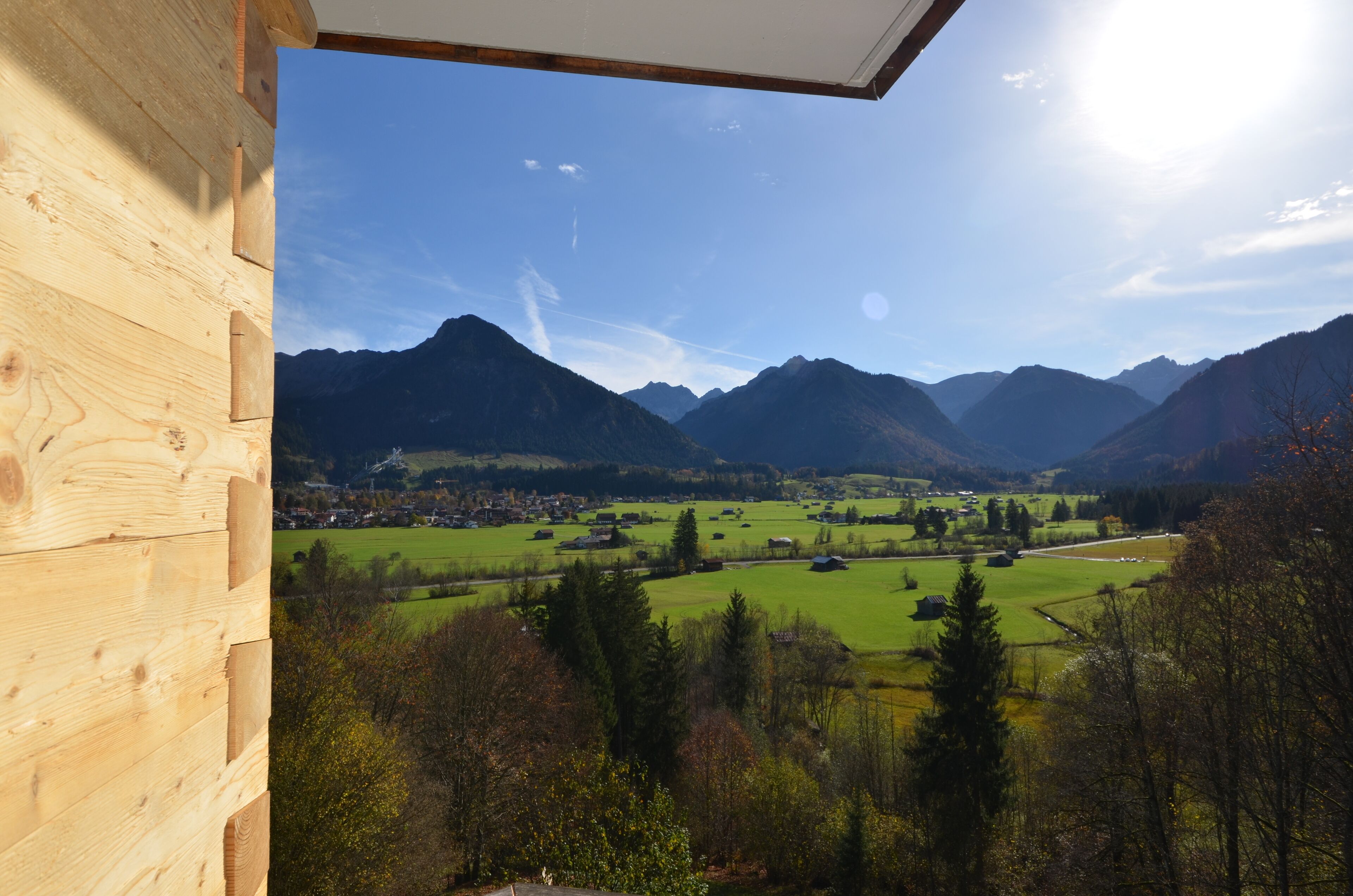 A wooden cabin with a view of a valley, mountains, and a clear sky.