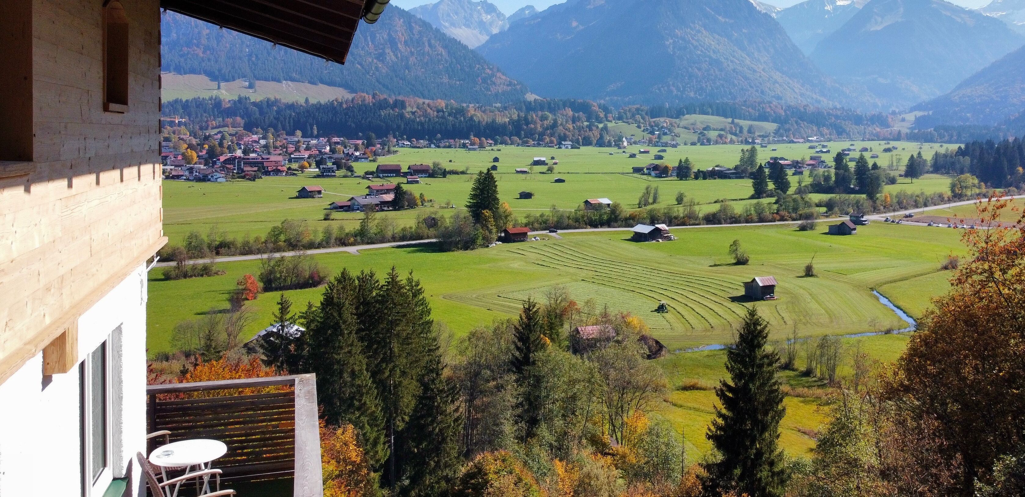 Vista desde un balcón sobre un paisaje rural con campos, casas y montañas.