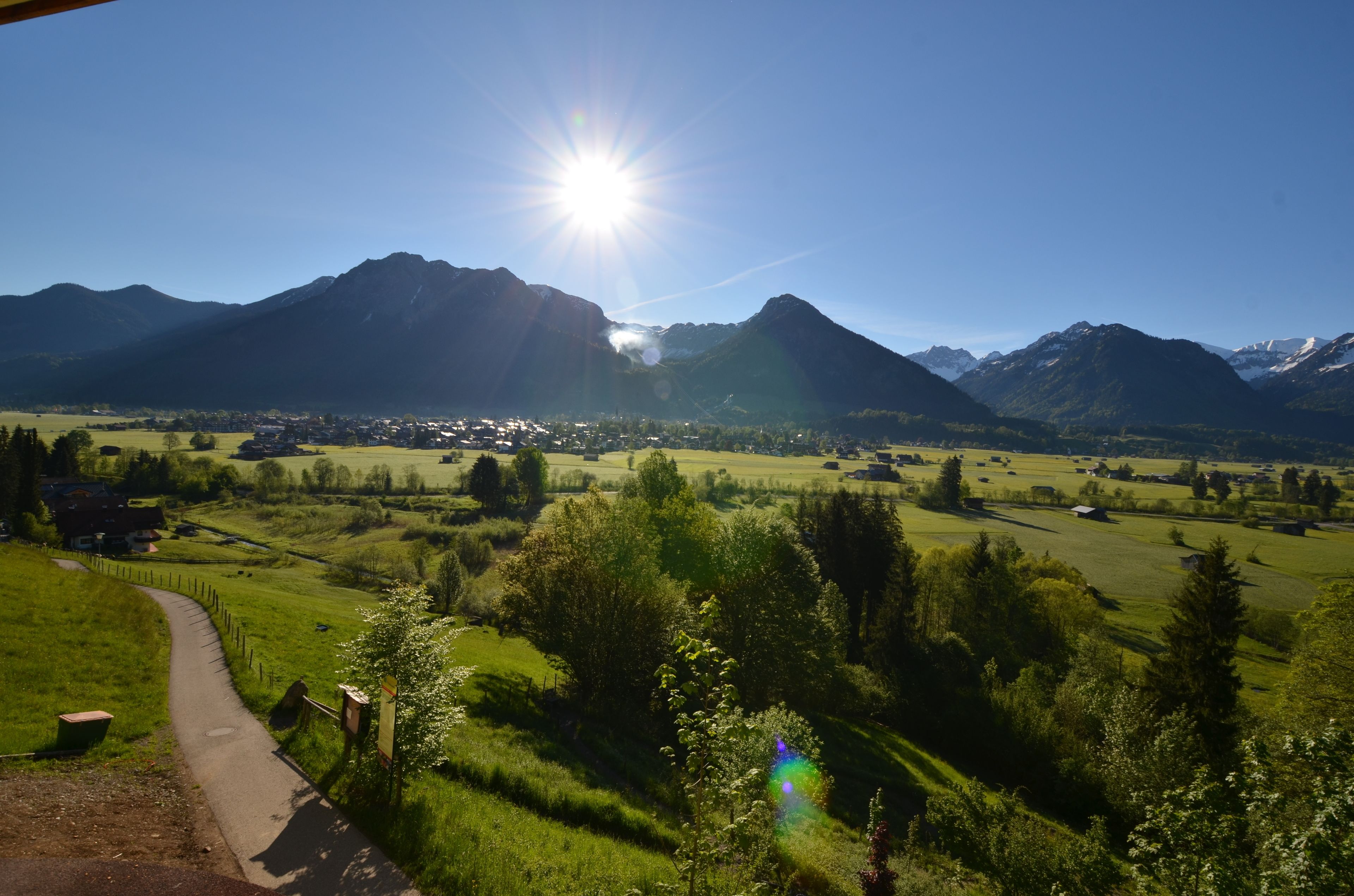 Un paysage rural avec des montagnes, un ciel dégagé et un sentier qui traverse une vallée verdoyante.