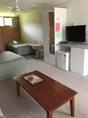 Una habitación pequeña con cama, un escritorio, televisor y refrigerador.