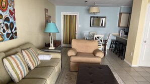 A living room with a beige sofa, striped pillows, a dark brown ottoman, a lamp, and a chair. - SUNDIAL - SITTING IN THE SAND. 3 BR, 2 BA. POOL. LESS CROWDED AREA OF BEACH. (Gulf Shores)