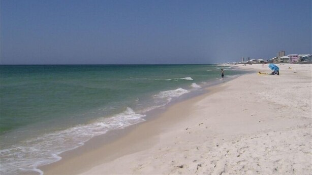 A beach with a clear sky, calm sea, and a few people. - SUNDIAL - SITTING IN THE SAND. 3 BR, 2 BA. POOL. LESS CROWDED AREA OF BEACH. (Gulf Shores)