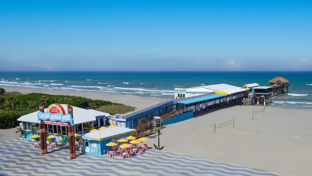 En strandbrygga med en restaurang som heter   ”Coco Beach Pier” och en byggnad med halmtak.