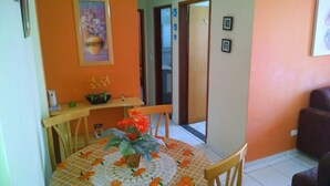 Zona pranzo con un tavolo rotondo ricoperto da una tovaglia con motivi arancioni e bianchi, un vaso con fiori arancioni e un quadro sopra il tavolo.