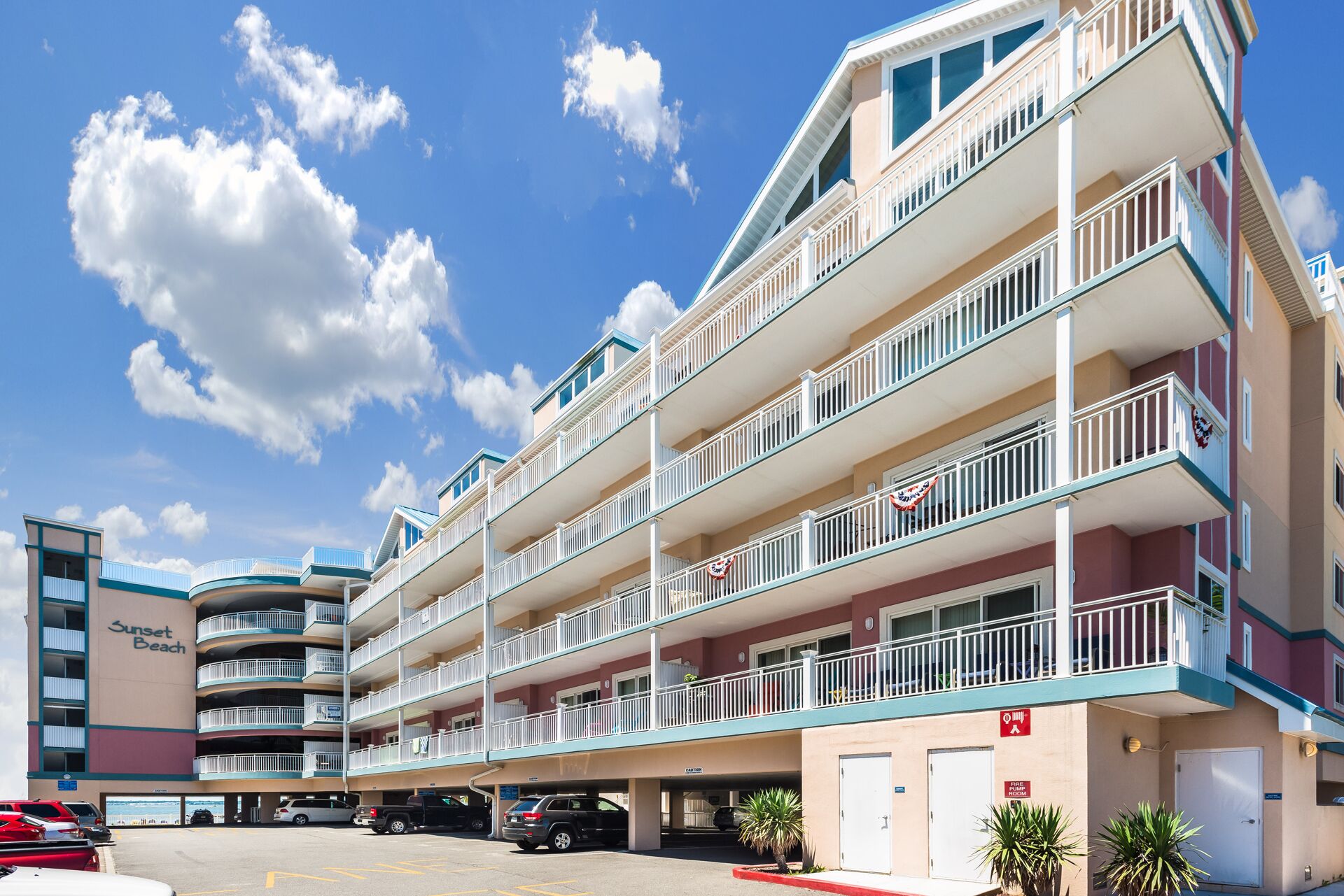 A multi-story hotel with balconies, a parking lot, and a beach view.