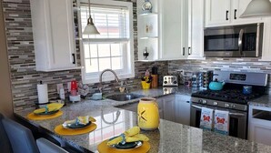 Una cocina moderna con encimeras de granito, armarios blancos, un microondas de acero inoxidable y una estufa a gas.