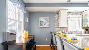 Una cocina moderna con encimera de granito, armarios blancos y un comedor con mesa y sillas de madera.