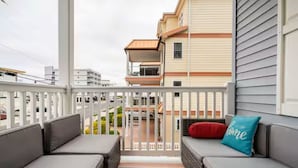Un balcón con mobiliario de mimbre y un tapete a rayas, con vistas a una zona residencial.