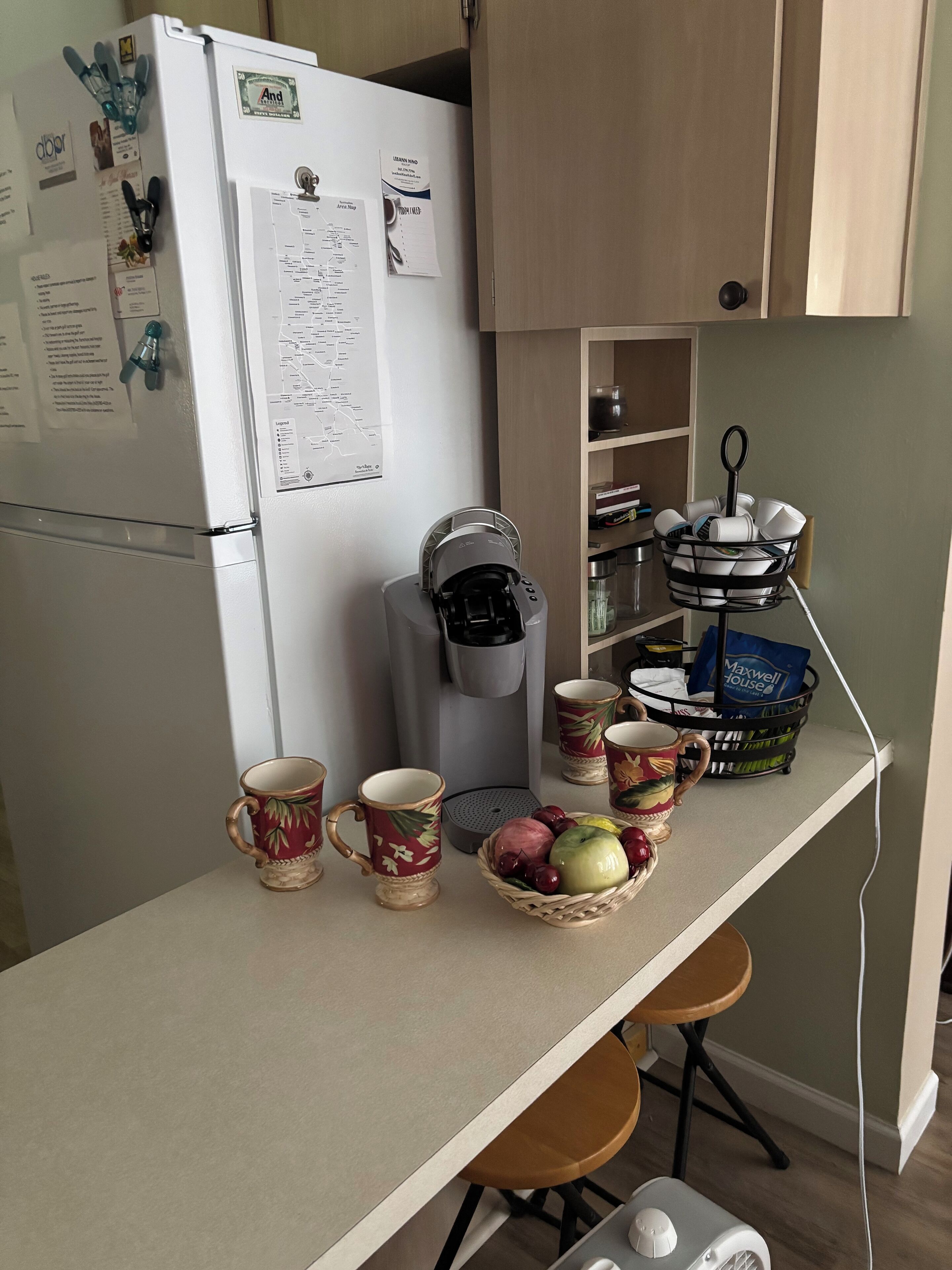 Eine Küche mit einem weißen Kühlschrank, einer Kaffeemaschine, einem Wäschekorb voller Geschirr und einer Obstschale auf der Arbeitsfläche.
