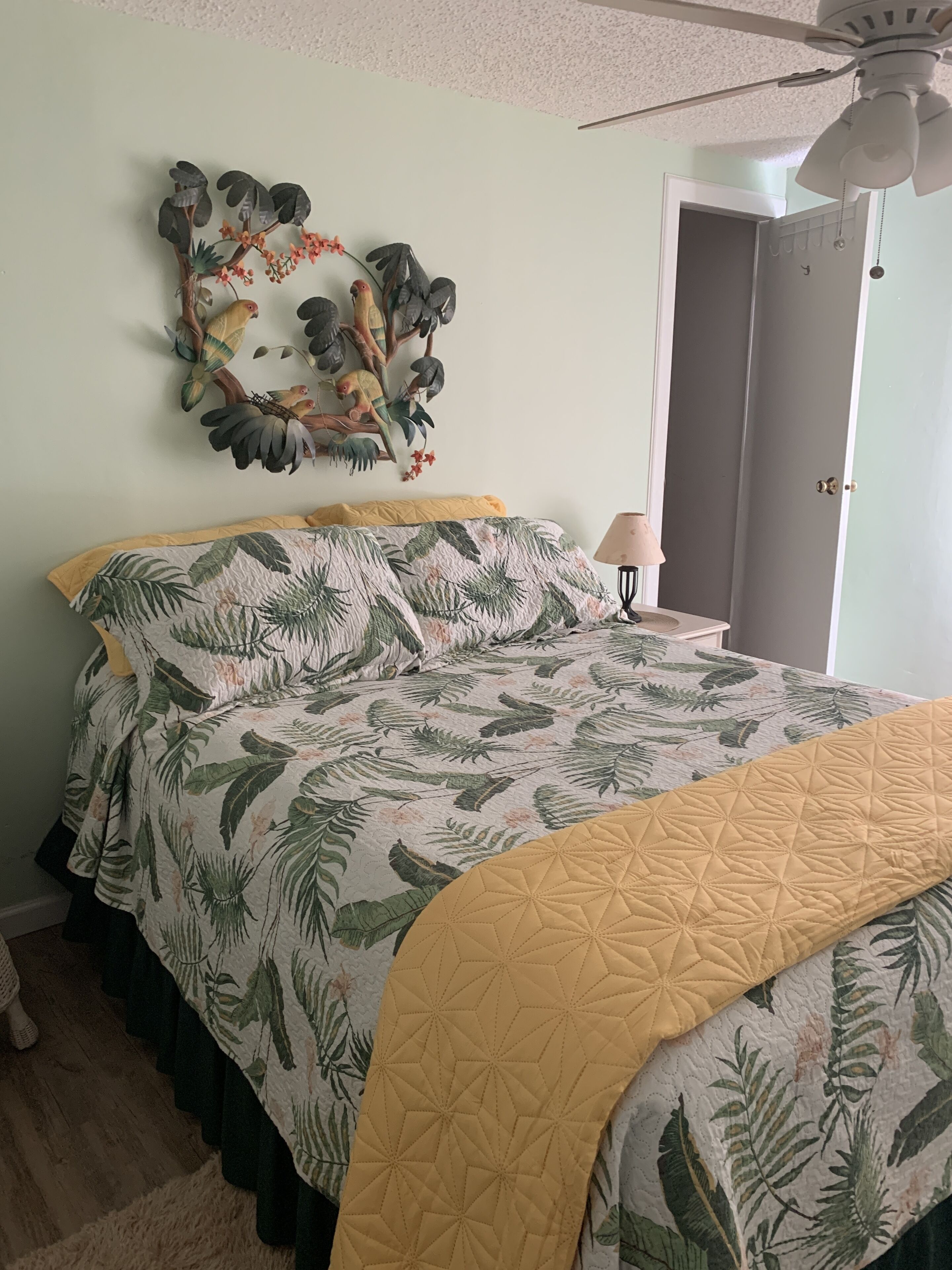 A bedroom with a bed, a ceiling fan, a door, and a wall decoration.