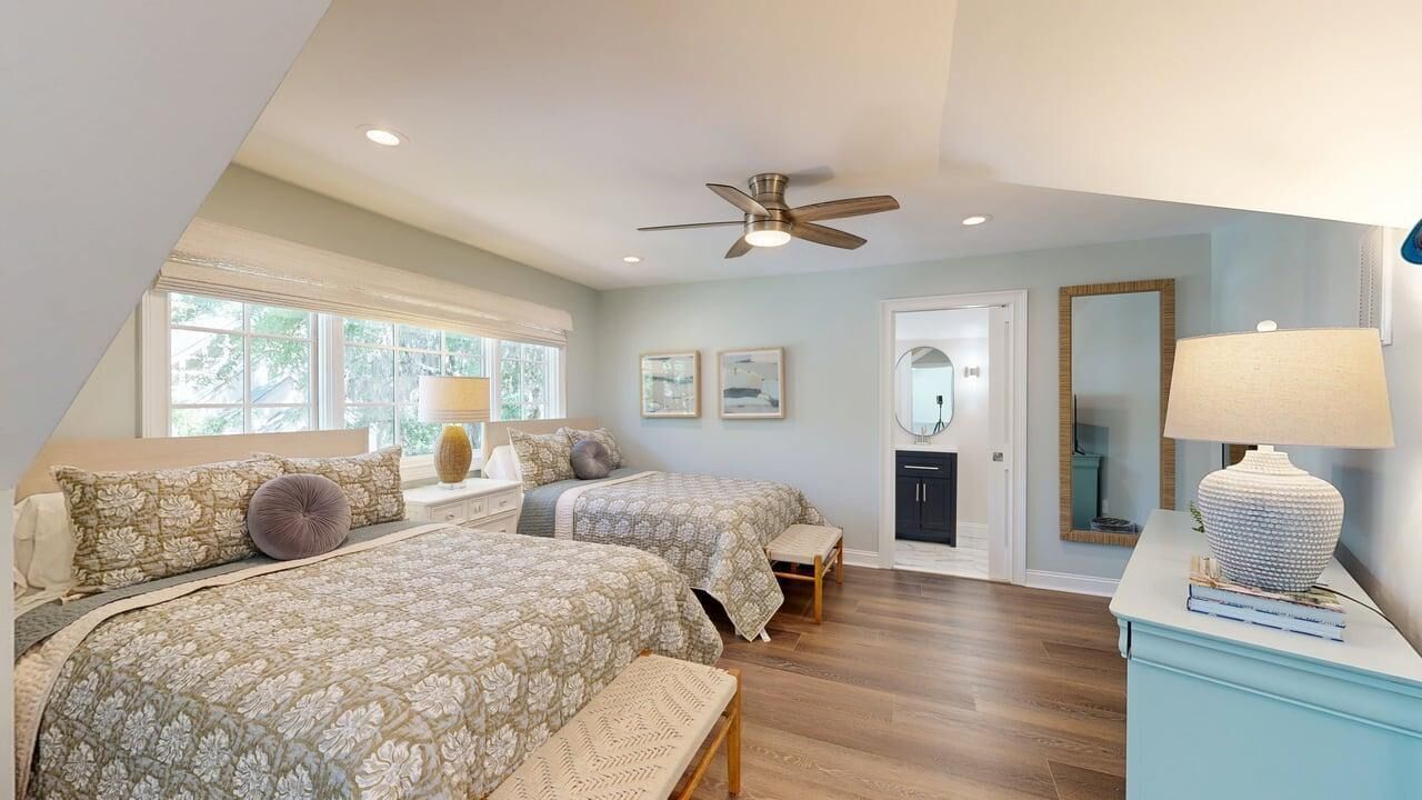 A bedroom with two beds, a ceiling fan, a door, and a window.