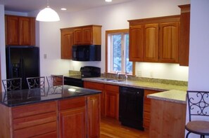 A kitchen with wooden cabinets, a black refrigerator, a microwave, a dishwasher, and a granite countertop. - Breathtaking New Premier Lake Champlain Waterfront Beach,Foliage,Ski Escape! (Addison)