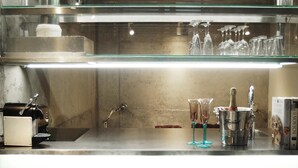 A bar area with a stainless steel counter, a coffee machine, and a wine cooler.