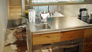 A modern kitchen with stainless steel appliances, a glass display case with wine glasses, and a cowhide rug on the floor.